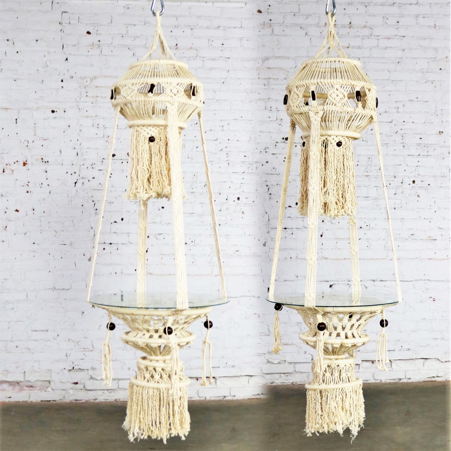 Beautiful pair of white cord macramé hanging tables with round glass tops. They are in wonderful age appropriate condition but not without minor flaws which do not take away from their overall look. Please examine photos. Circa 1960s-1970s.